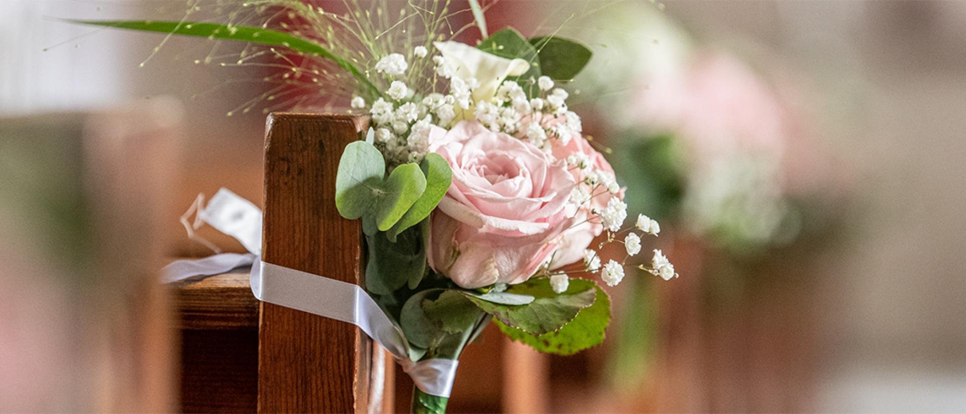 Een boeket van roze bloemen met op de achtergrond wazig afgebeeld roze bloemen aan kerkbanken.