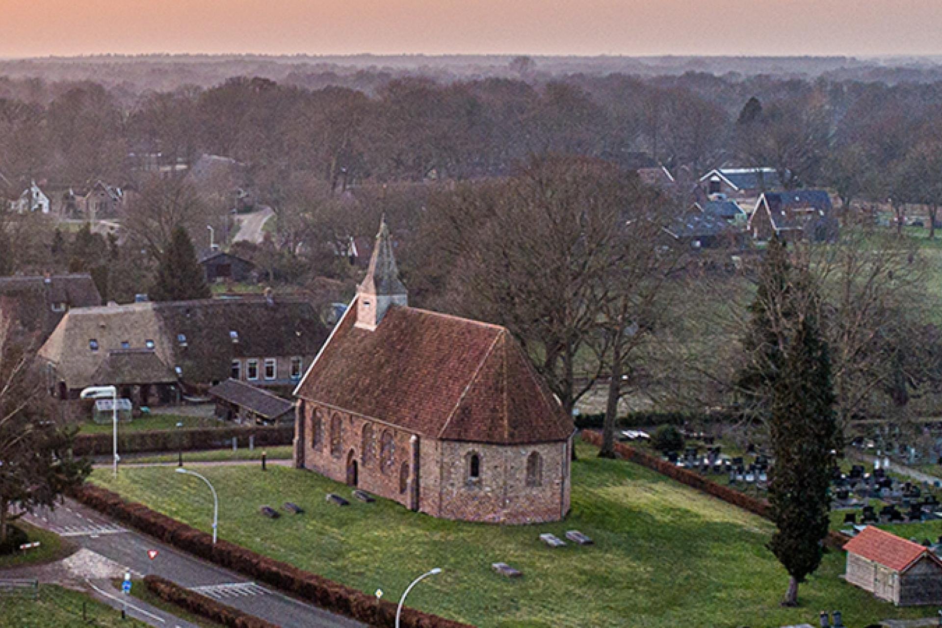 Landschap met kerkje Zweeloo en aan de rechterkant deel begraafplaats, aan de horizon oranje gloed zonsondergangLuchtfoto van het kerkje van Zweeloo tijdens zonsondergang 