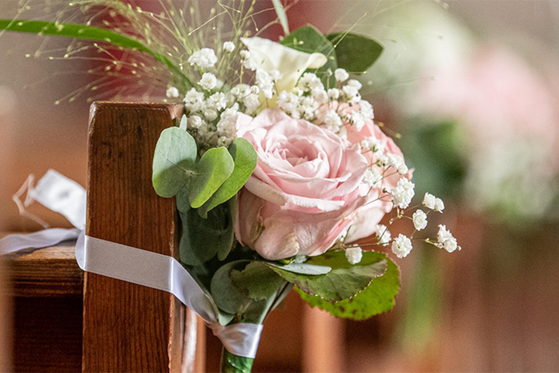 Een boeket van roze bloemen met op de achtergrond wazig afgebeeld roze bloemen aan kerkbanken.