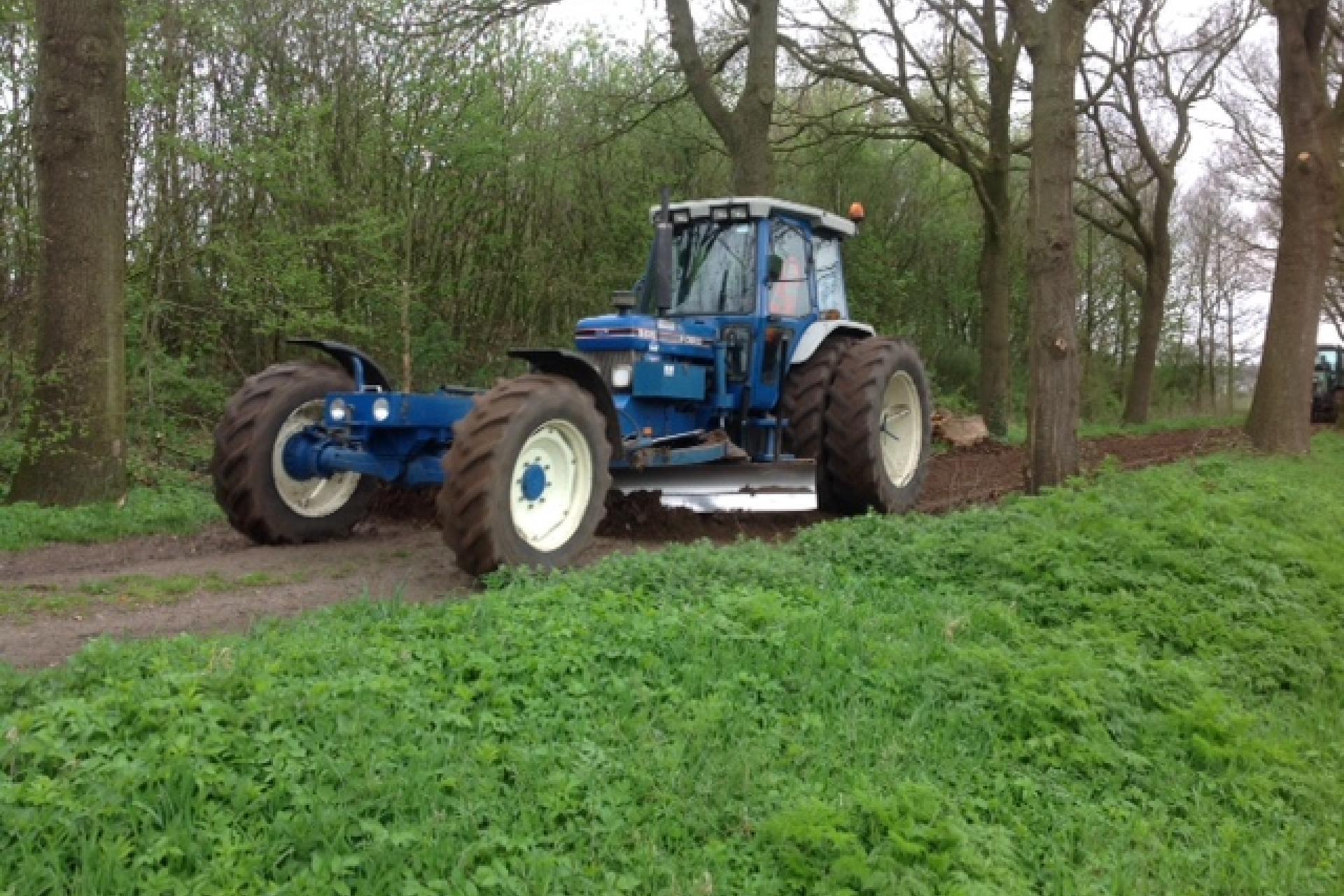 Een blauwe tractor hersteld de zandwegen in de Gemeente Coevorden